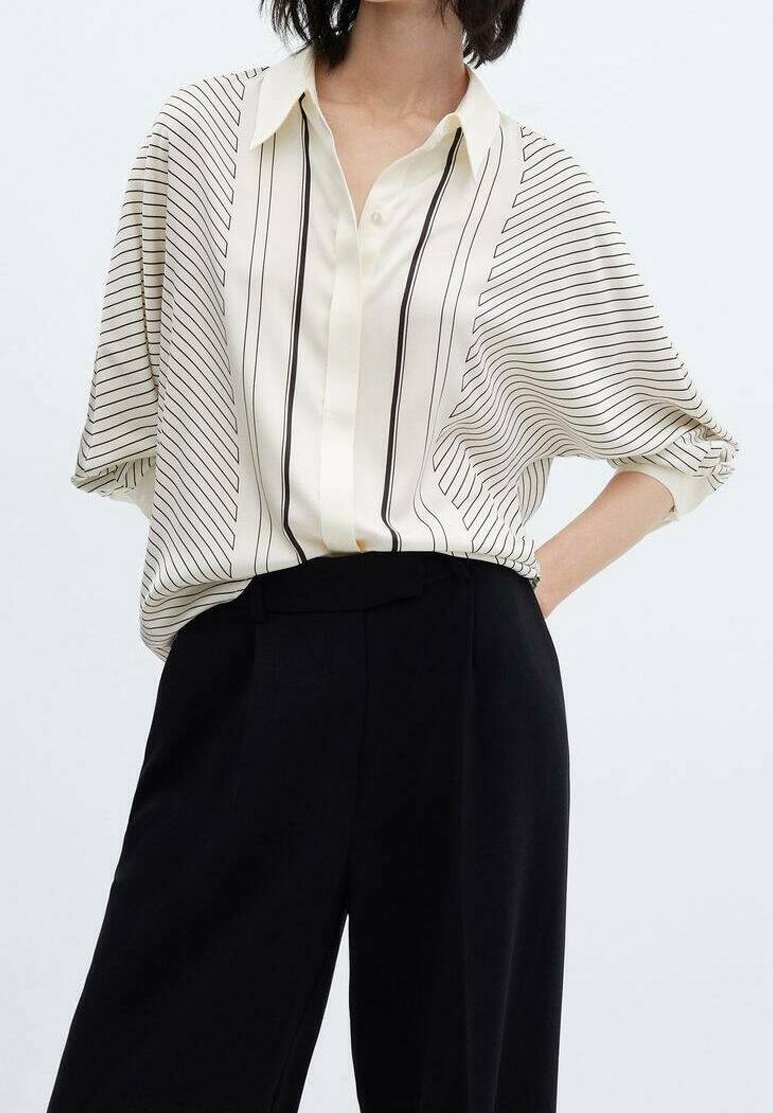 Hellbeige Bluse mit schwarzen, vertikalen Streifen, mit einer Knopfleiste und einem lässigen Schnitt. Kombiniert mit maßgeschneiderten schwarzen Hosen.
