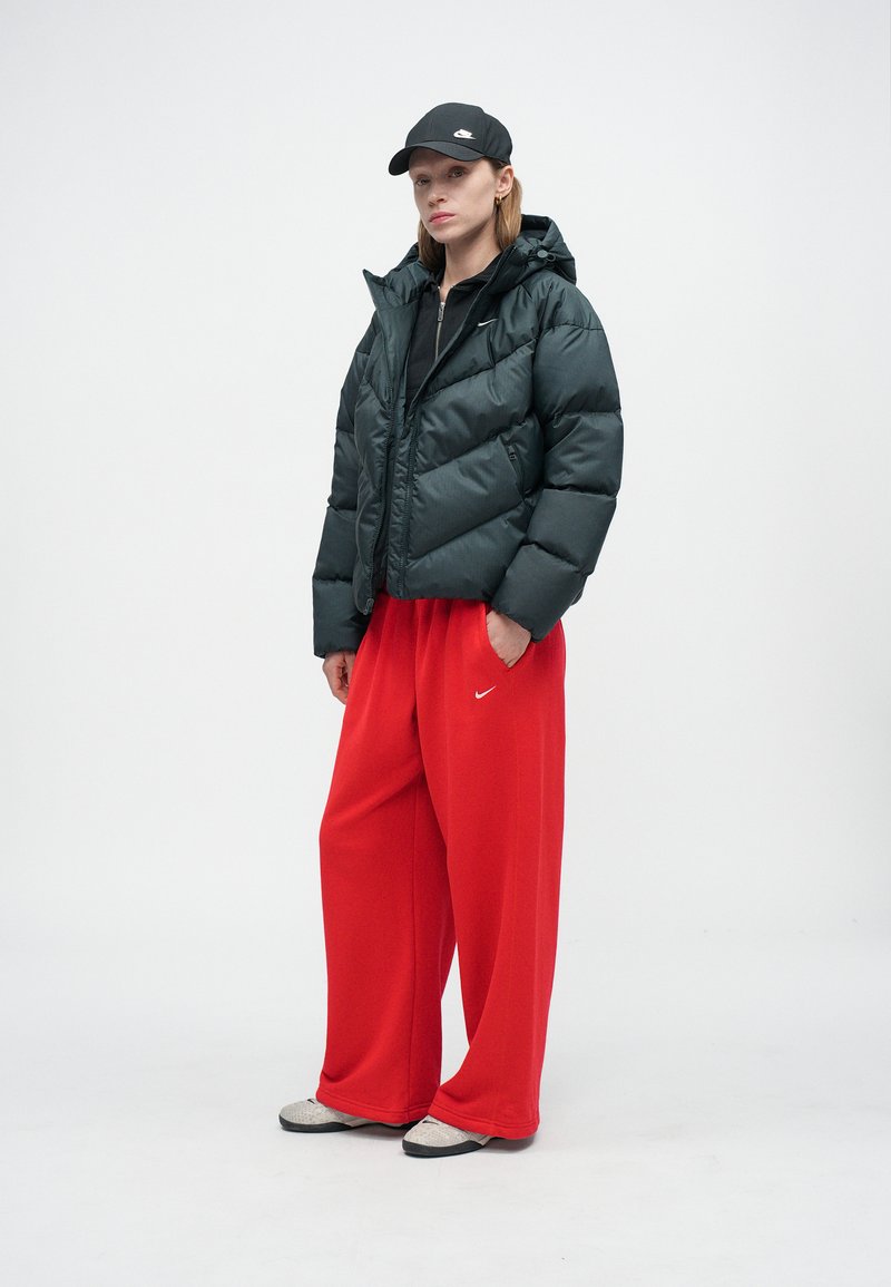 Black puffer jacket with hood, red wide-leg sweatpants, grey shoes, and a black cap. The jacket has a shiny texture and zip closure.