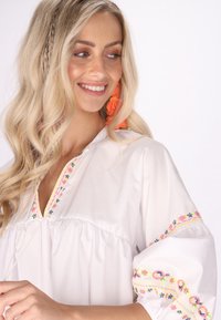 Bluză albă cu mâneci bufante, având broderie florală colorată de-a lungul gâtului și mânecilor, confecționată dintr-un material ușor și neted.