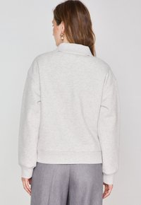 Sweatshirt gris clair avec un col, des épaules tombantes et des poignets côtelés. Tissu doux avec une coupe décontractée, associé à un pantalon gris.