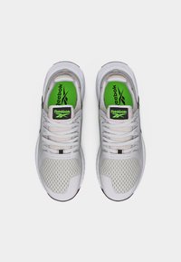 Ζευγάρι ανοιχτόχρωμων γκρι αθλητικών παπουτσιών Reebok με λευκά κορδόνια και πράσινες σόλες, σε θέα από πάνω σε λευκό φόντο.