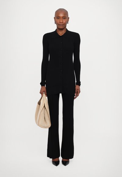 Černé žebrované šaty s dlouhým rukávem a límečkem, s knoflíkovým zapínáním, v kombinaci s rozšířenými černými kalhotami a béžovou kabelkou.