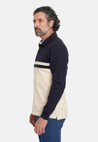 Polo de manga larga en navy y crema, con un diseño a rayas en el pecho, el cuello y las aberturas laterales. Material de algodón.