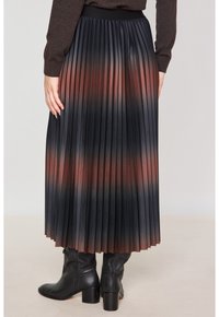 Jupe plissée noire avec un dégradé de rouge profond. Dispose d'une finition texturée et d'une taille élastique, assortie à des bottes noires montantes.