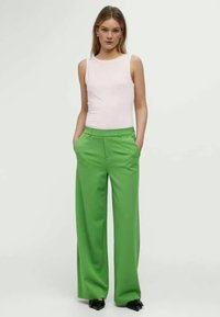 Green wide-leg trousers with a high waist and pleats, paired with a fitted light pink tank top. Smooth fabric with a tailored fit.