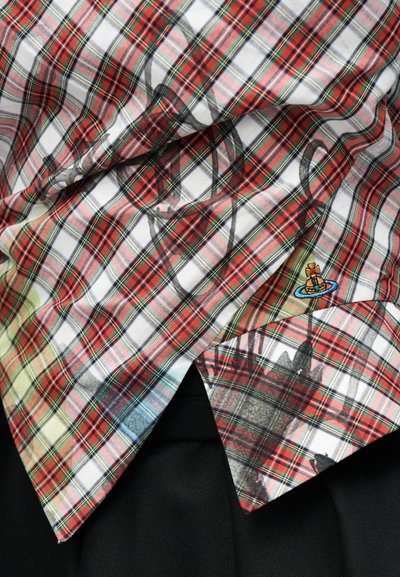 Ύφασμα με καρό σε κόκκινο, λευκό και πράσινο, με μαύρο αφηρημένο μοτίβο και ένα μικρό κεντημένο κίτρινο και μπλε έμβλημα σε μαύρο φόντο.