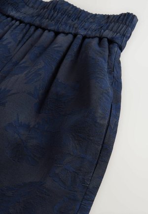 Mörkblå shorts med elastisk midja, prydda med ett texturerat blommönster och en slät finish, vinklade för att visa drapering och design detaljer.