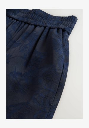 Tumed sinised lühikesed püksid elastse vöökohaga, millel on tekstuuriga lillemuster ja siledad viimistlused, kallutatud, et näidata langemist ja disaini detaile.