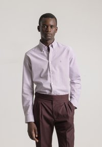 Camisa de botones a rayas en púrpura claro y blanco, hecha de algodón, combinada con pantalones oscuros de burdeos con pliegues. Textura suave, diseño de cuello clásico.