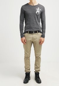 Mörkgrå långärmad tröja med vitt grafik, kombinerad med beige byxor och svarta snörskor, med en slät textur och sågtad passform.