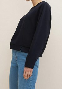 Marinblå ribbad tröja i stickad kvalitet med långa ärmar, cropped nederkant, rund halsringning och avslappnad passform, kombinerad med ljusblå denimjeans.