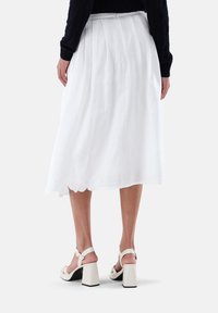 Gonna midi bianca plissettata con ricami floreali all'orlo, abbinata a sandali con tacco a blocco beige. Tessuto testurizzato, design elegante.