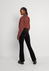 Rode en bruine geruite blouse met lange mouwen en een kraag, gecombineerd met zwarte fluwelen flared broek en zwarte platformlaarzen.