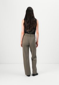 Pantalons taille haute vert olive avec une coupe décontractée, dotés d'une ceinture texturée et de jambes droites, associés à un haut en dentelle noire.