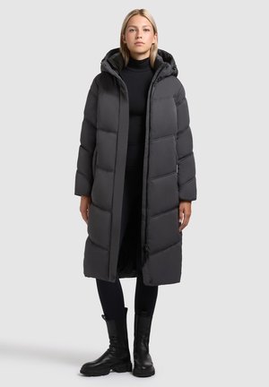 Long, puffy black coat with horizontal stitching, a hood, and front zipper. Worn over a black top and leggings, paired with black ankle boots.