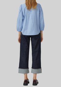 Lichtblauw gestreepte blouse met pofmouwen, gecombineerd met donkerdenim wijde broek met opgerolde boorden en zwarte schoenen met glanzende afwerking.