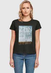 Must musta särk, millel on ristkülikukujuline graafiline print, millel on tekst "ZAYN" ja maastiku stseen. Lühikesed varrukad ja vabam lõige.