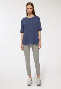 T-shirt blu a maniche corte in cotone abbinato a pantaloni della tuta grigi chiari, a gamba tapered, con orlo arrotolato e design aderente. Sneakers argento completano il look.