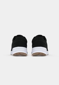 Ein Paar schwarze Sportschuhe mit weißen Sohlen, von hinten auf einem schlichten hellen Hintergrund gezeigt.