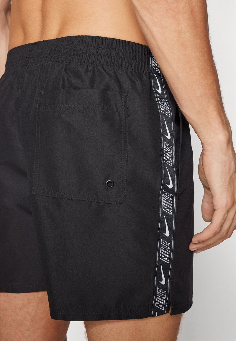 Pantaloni da bagno neri con vita elastica, strisce laterali con il testo "NIKE" e una tasca sul retro con un dettaglio a foro.