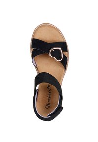 Sandalia negra con tiras cruzadas, detalle metálico en forma de corazón, plantilla acolchada en tono marrón y costuras blancas a lo largo de la suela.