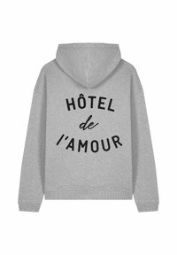 Szürke kapucnis pulóver fekete "HÔTEL de l'AMOUR" felirattal a hátsó részén, ívelt elrendezésben.