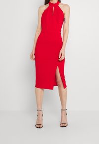 Röd halterneck-klänning med ett nyckelhålssnitt, figursydd silhuett, knälång med split på sidan, tillverkad av ett smidigt tyg.