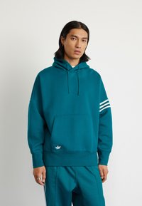 Felpa di colore teal con tasca frontale, cappuccio con cordino e tre strisce bianche sulla manica destra. Presenta un piccolo logo bianco all'orlo.