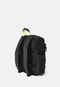 Black nylon backpack with a textured back panel, adjustable straps, side pockets, and a bright green top handle for easy carrying.