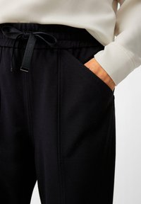 Black sweatpants with a drawstring waist, featuring side pockets, a smooth texture, and contrasting stitching details.