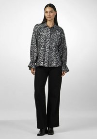 Leopardmønster button-up skjorte i grå og sort, med lange ærmer der har flæser ved manchetterne. Parret med sorte bukser med vidde og ankelstøvler.
