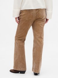 Brown corduroy flared pants with visible pockets and a textured finish. Worn with a white, knit long-sleeve top and brown heeled boots.