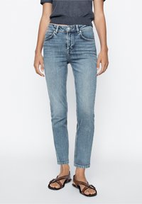 Jean en denim bleu clair avec une coupe droite, design à cinq poches et léger effet froissé. Associé à des sandales noires.