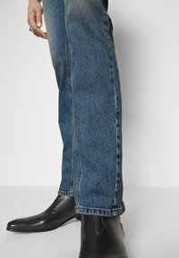 Jeans de mezclilla azul oscuro con un corte recto, combinados con elegantes botas de cuero negro hasta el tobillo. Los jeans cuentan con costuras en contraste y bolsillos estándar.