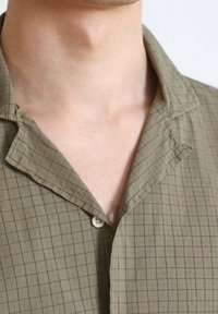 Short-sleeve shirt in khaki cotton with a grid pattern, featuring a notched collar and a single button closure near the neck.