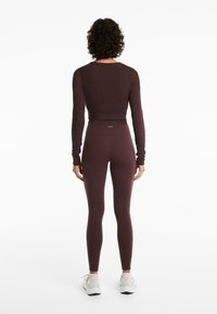 Burgundivörös, hosszú ujjú felső és hozzá illő, magas derekú leggings, rugalmas, texturált anyagból készült. Fitt sziluett és egyszerű design jellemzi.