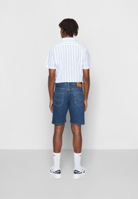 Camisa de mangas curtas às riscas em branco e azul claro, combinada com calções de ganga azul escura, meias brancas e sapatilhas.