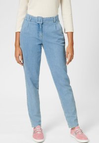 Hellblaue Jeanshosen mit tailliertem Bund, zulaufenden Beinen und vorderen Falten, kombiniert mit pinken Sneakers mit silbernen Akzenten.