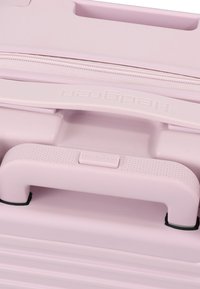 Poignée et fermeture éclair rose clair de la valise avec prise texturée et logo "Hedgren" embossé sur la poignée.