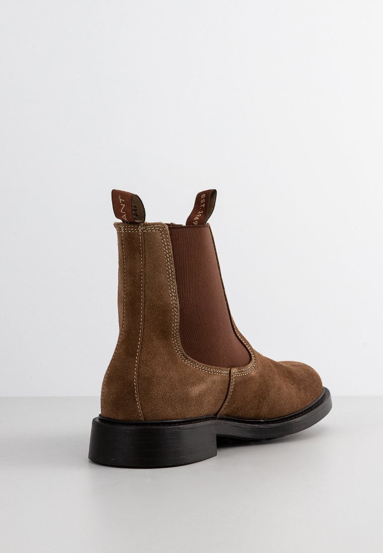 Brązowe zamszowe botki za kostkę z elastycznymi panelami po bokach, zaokrąglonym noskiem i czarną gumową podeszwą. Posiadają pętelkę z tyłu.