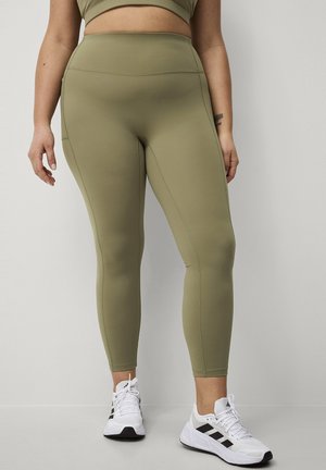 Olijfgroene high-waisted leggings van glad, rekbaar materiaal met platte naden, gecombineerd met witte sportschoenen.