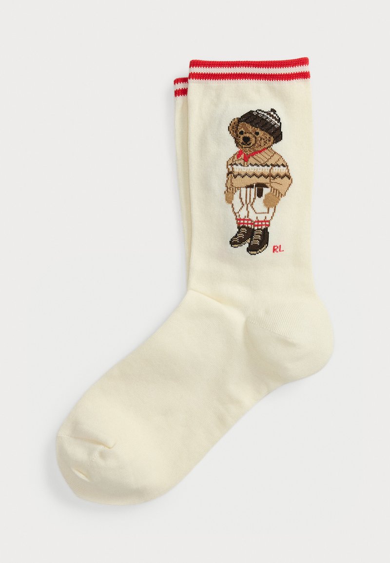 Calzino crema con strisce rosse sulla parte superiore e un orso marrone che indossa un maglione a strisce, un berretto, pantaloni bianchi e stivali lavorati a maglia sul lato.