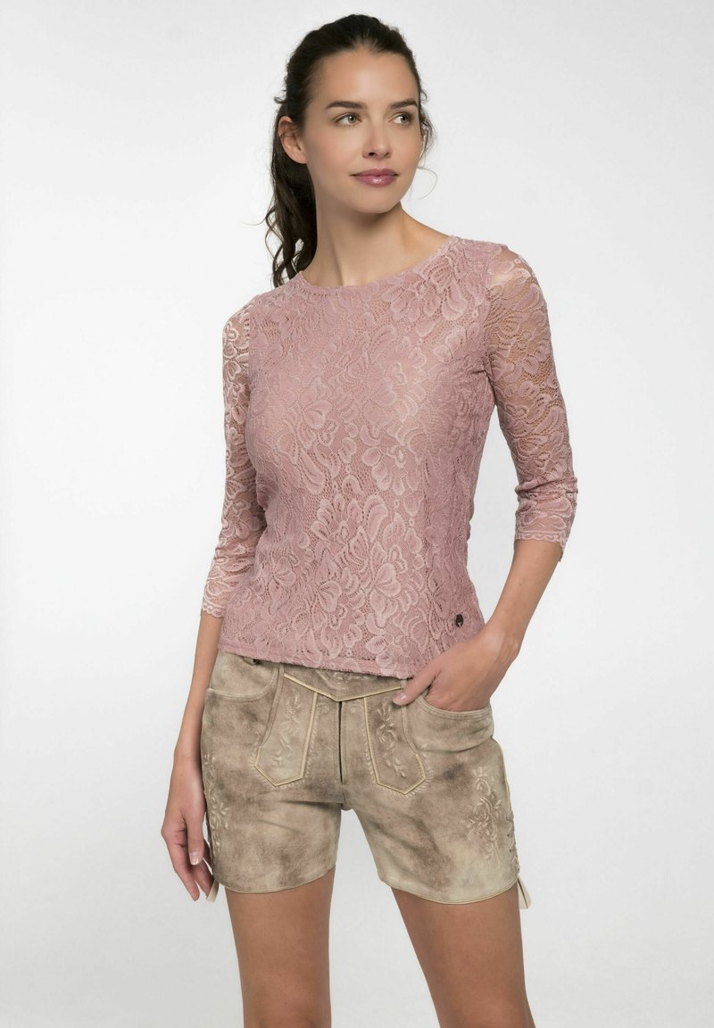 Spitzenoberteil in staubigem Rosaton, mit langen Ärmeln und floralen Mustern, kombiniert mit hellbraunen, leicht verwaschenen Shorts mit Stickerei.