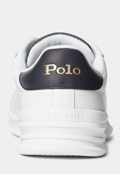 Baskets blanches avec languette de talon bleu marine portant le texte doré « Polo » et embossage « Ralph Lauren » sur la semelle blanche, vues de dos.