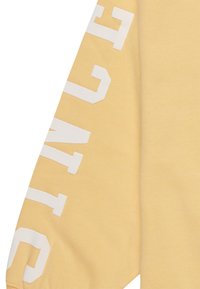 Sudadera amarilla con texto blanco en negrita a lo largo de la manga. La tela parece suave, con una textura lisa y un ajuste relajado.