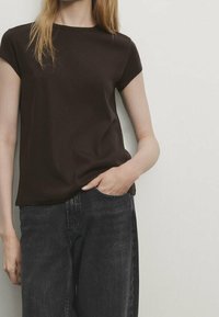 Maglietta corta marrone scuro con collo a giro, realizzata in tessuto morbido. Abbinata a jeans neri a vita alta, che presentano una vestibilità morbida.