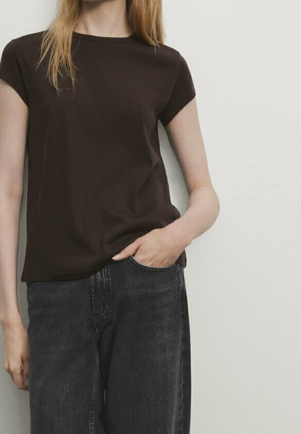 Maglietta corta marrone scuro con collo a giro, realizzata in tessuto morbido. Abbinata a jeans neri a vita alta, che presentano una vestibilità morbida.