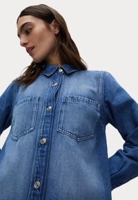 Jeansowa koszula w jasnoniebieskim kolorze, z długimi rękawami, zapięciem na guziki z przodu, dwiema kieszeniami na piersi oraz klasycznym kołnierzykiem. Gładka tekstura z metalowymi guzikami.