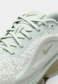 Sneaker Nike verde chiaro con tomaia texturizzata, chiusura con lacci, dettagli dorati e suola imbottita con air cushion visibile.