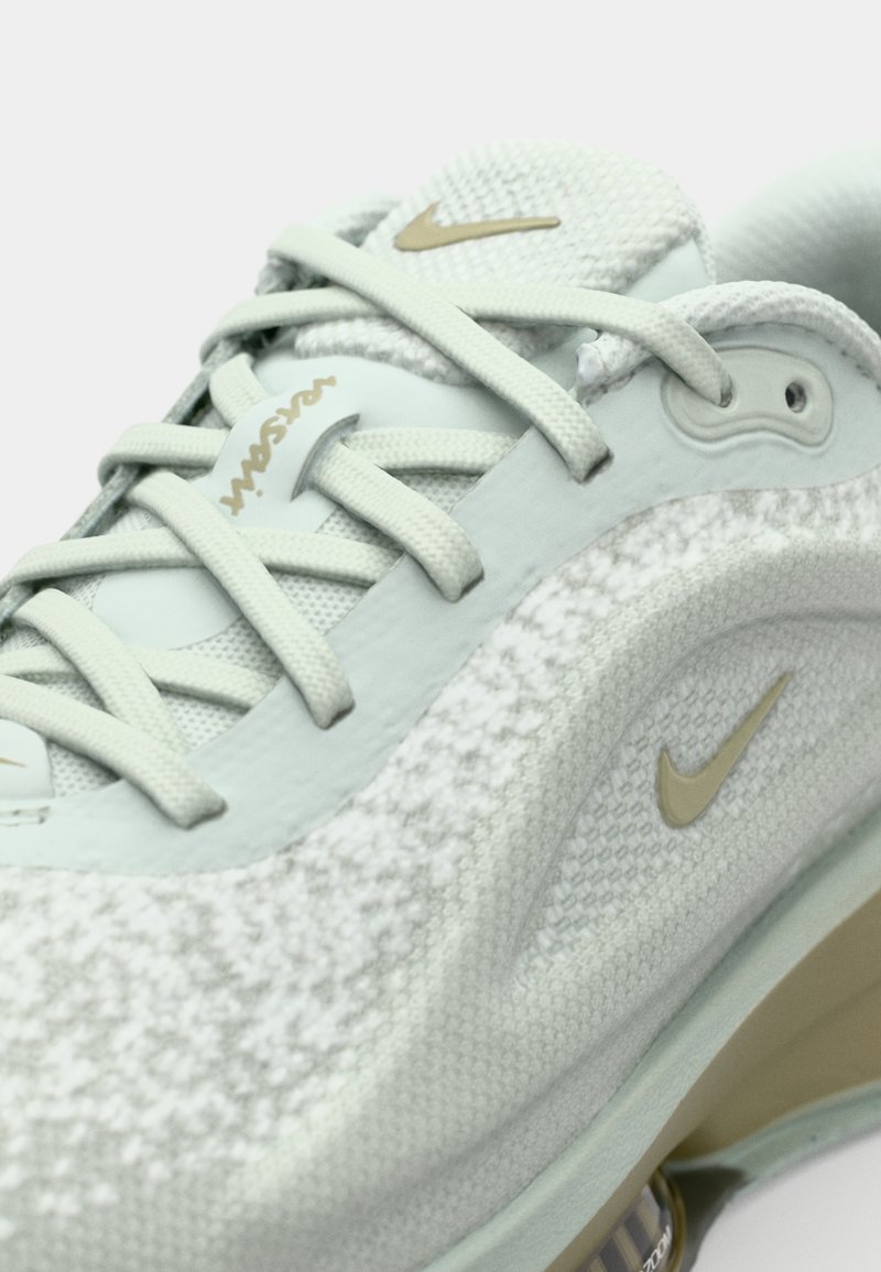 Zapatilla Nike verde clara con parte superior texturizada, cierre de cordones, detalles en dorado y suela acolchada con amortiguación de aire visible.